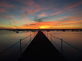 Sunset over a pier with boats in the harbor