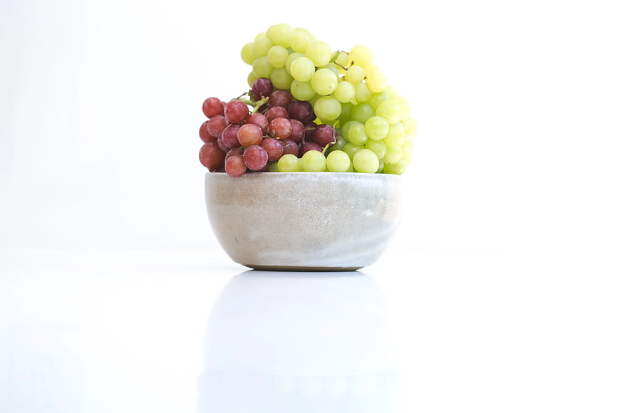 Fresh Green and Red Grapes in Ceramic Bowl on White
