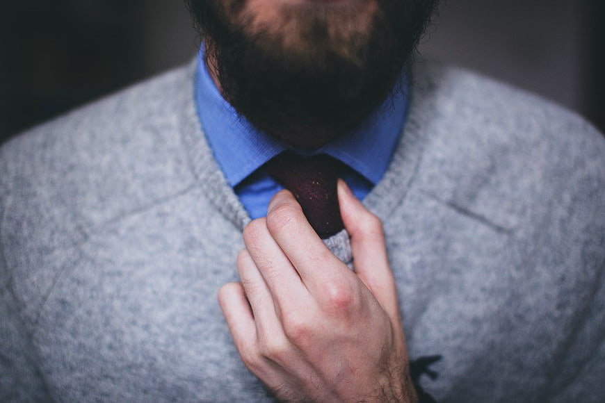 Close-up of man adjusting tie in grey sweater
