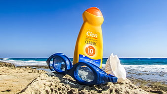 Sunscreen bottle and blue swimming goggles on a sandy beach