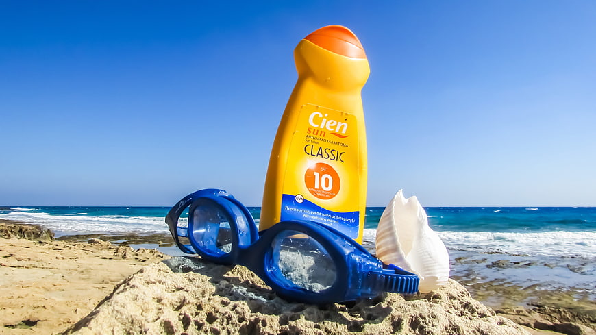 Sunscreen bottle and blue swimming goggles on a sandy beach
