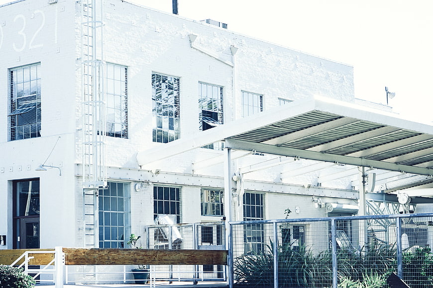 White industrial warehouse building with metal awning and fence