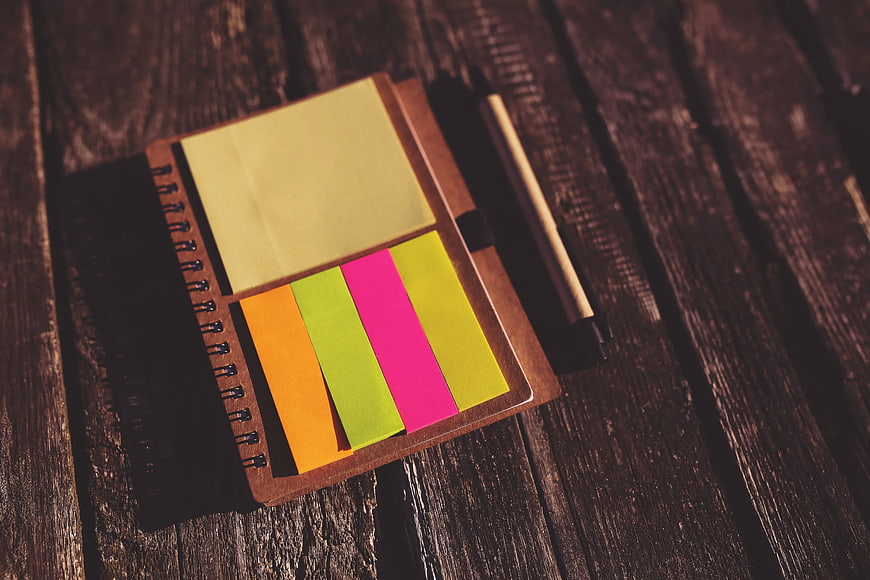Colorful sticky notes on notebook with pen on wooden table