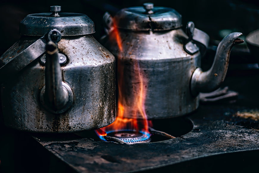 Two weathered metal kettles on a gas stove with flame