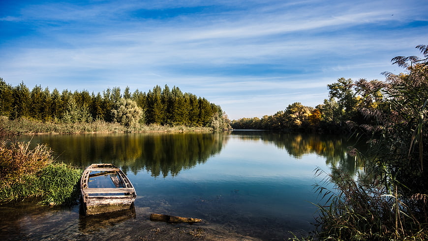 Old wooden boat on calm river bank with forest reflection