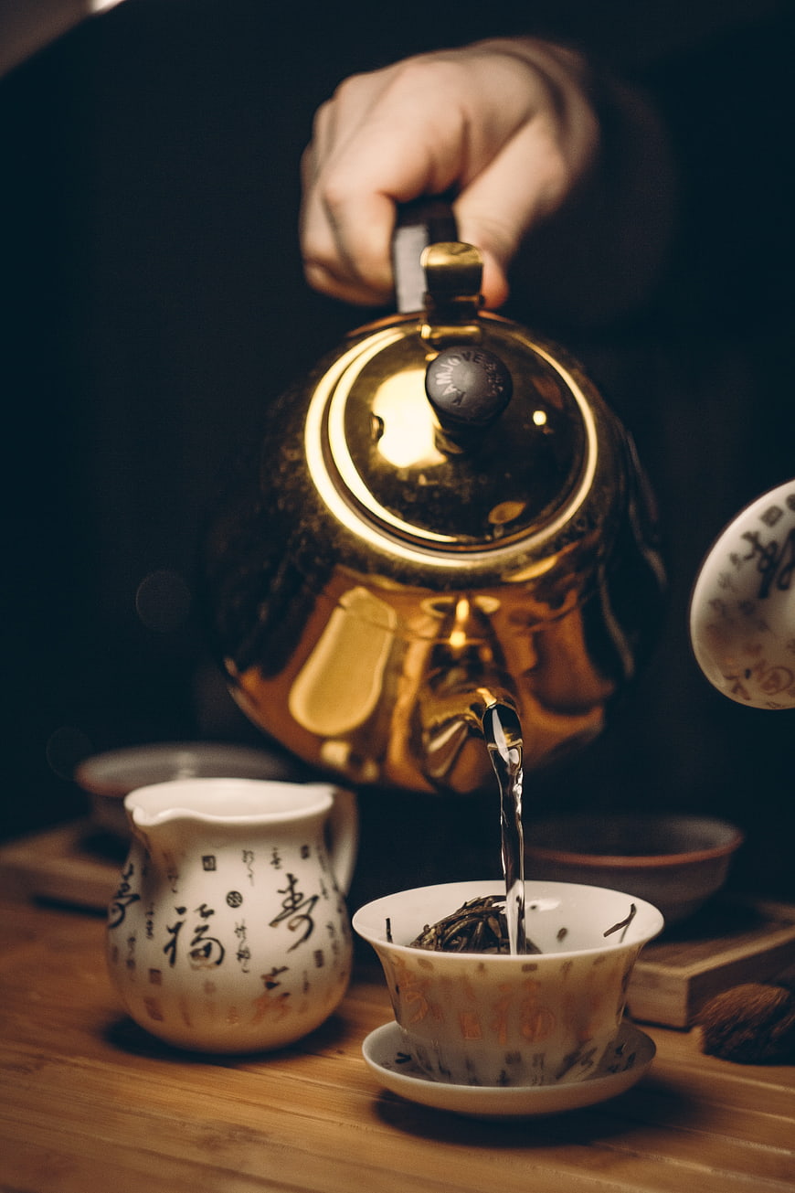 Pouring hot water from brass teapot into traditional tea cup