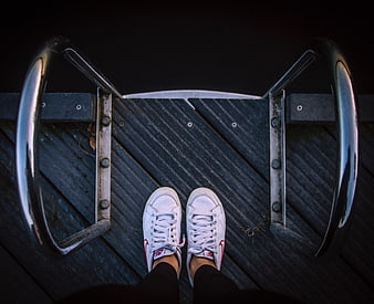 First-person view of white sneakers on metal bike rack