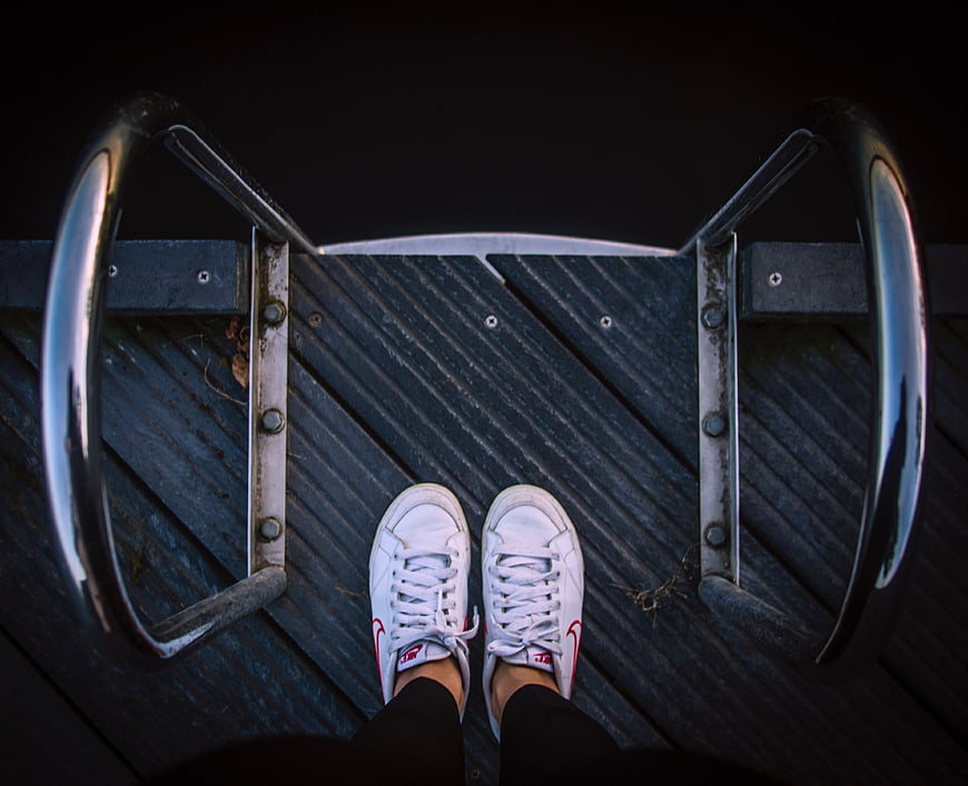 First-person view of white sneakers on metal bike rack