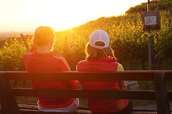 Two women relaxing on a bench in a vineyard at sunset