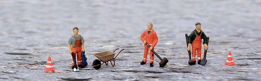 Miniature construction workers on wet asphalt road