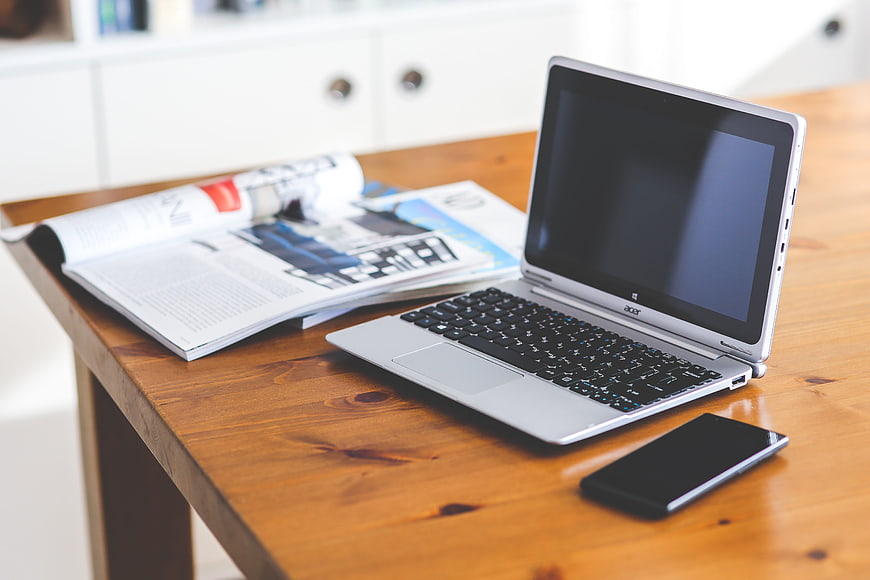 Silver laptop, smartphone, and magazine on wooden desk workspace