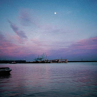 Starry night sky over harbor with boat and cranes