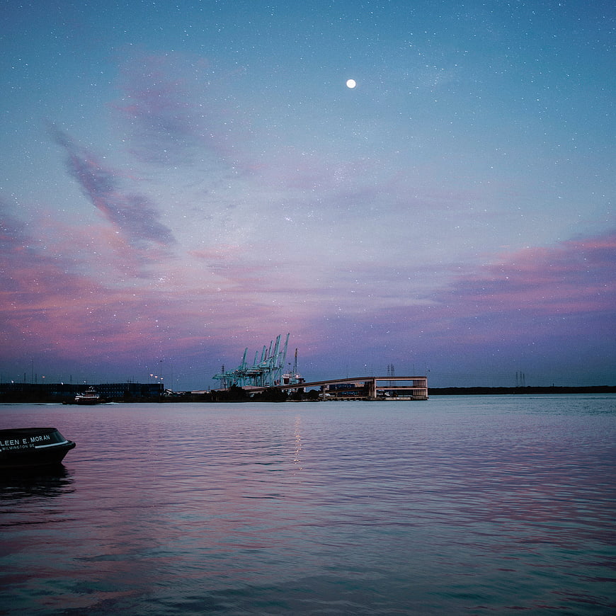 Starry night sky over harbor with boat and cranes