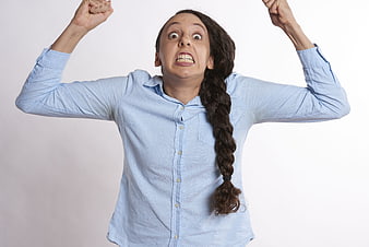 Frustrated young woman with braided hair raising fists in anger
