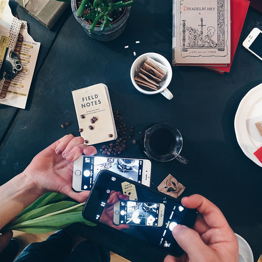 Top view of hands photographing coffee and notebook with smartphones
