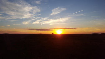 Sunset over a dark landscape with wispy clouds