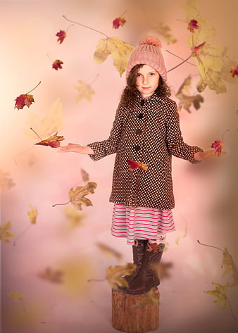 Cute girl in autumn coat standing on stump with falling leaves