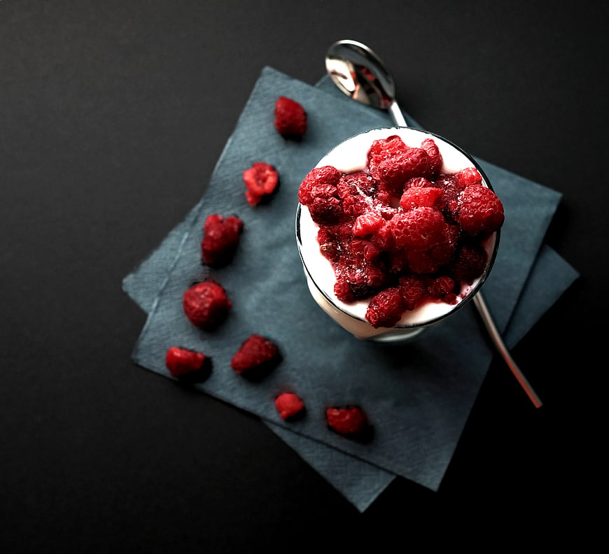 Overhead view of raspberry yogurt dessert with spoon on dark background