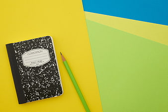 Composition notebook and green pencil on colorful background