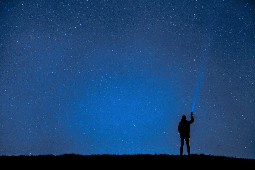 Silhouette of Person with Flashlight Under Starry Night Sky