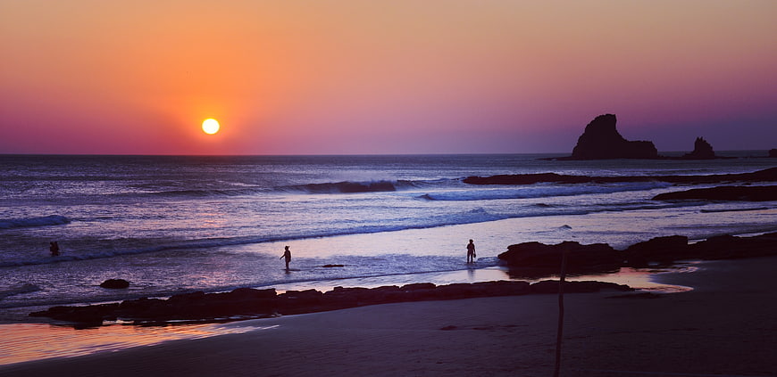 Silhouetted Figures on Beach at Sunset with Ocean Waves