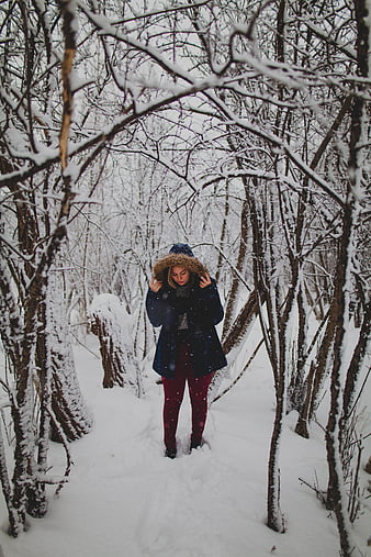 Woman in winter coat walking through snowy forest path