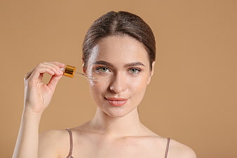 Woman applying serum dropper to face for skincare
