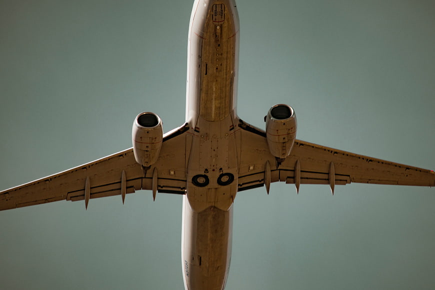 Low angle view of airplane belly flying overhead against blue sky