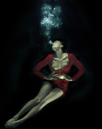 Underwater fashion portrait of a woman in a red dress with rising bubbles