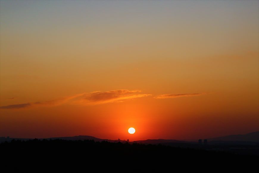 Vibrant orange sunset over dark silhouette landscape