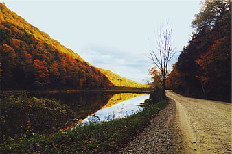 Scenic gravel road alongside lake with autumn forest hills