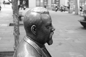Black and white profile of a bronze bust statue in a city square