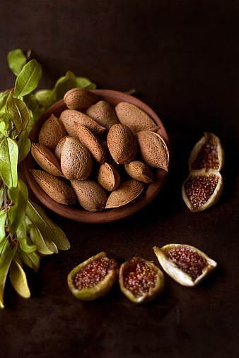 Almonds in clay bowl with fresh figs and green leaves
