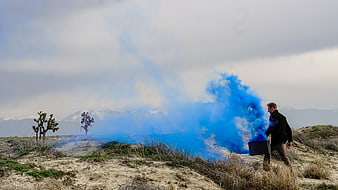 Man with Blue Smoke Bomb in Desert Landscape