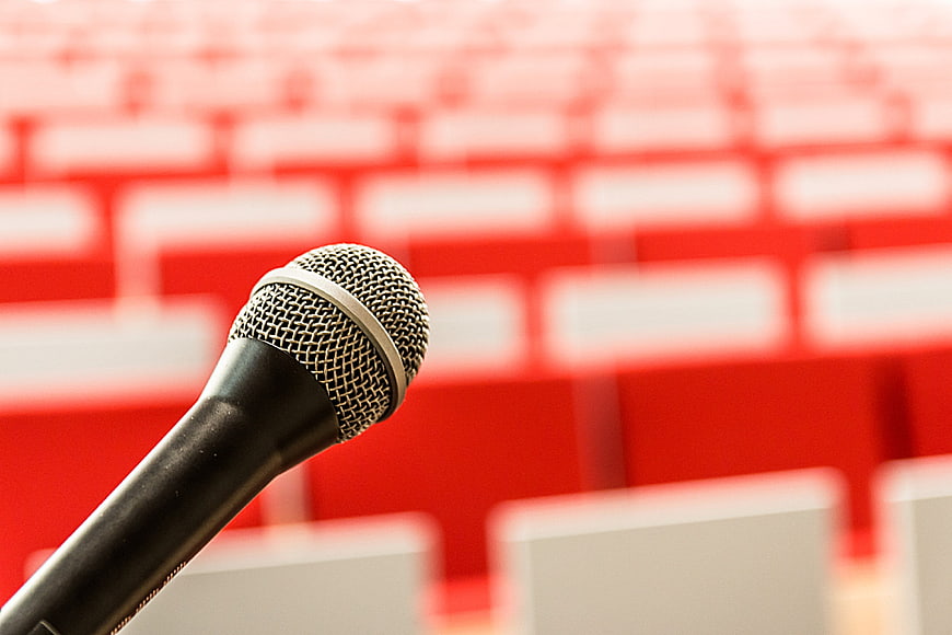 Close-up of microphone in front of blurred red lecture hall seats