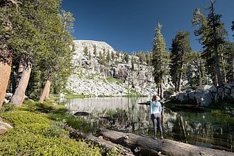 Woman hiking by alpine lake with granite cliffs and pine trees
