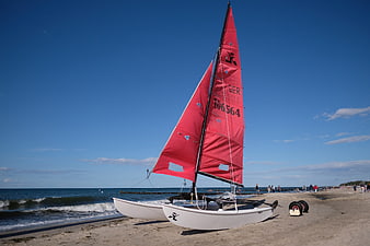 Red sailboat on sandy beach with blue sky
