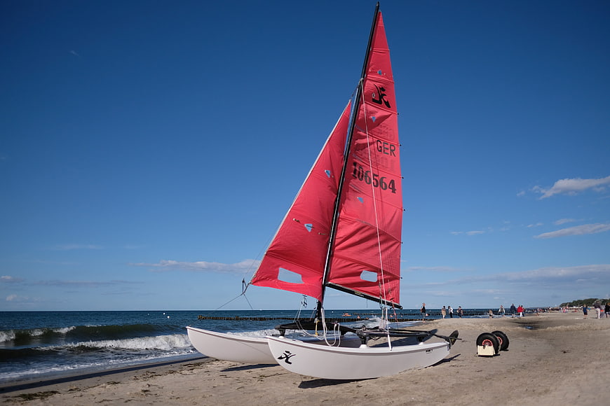 Red sailboat on sandy beach with blue sky