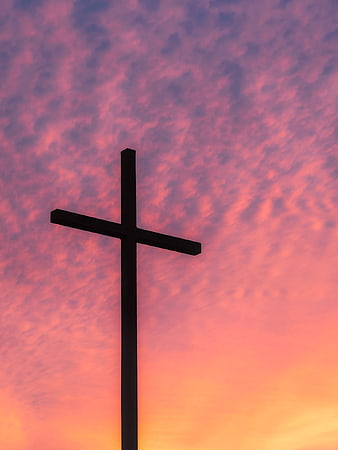 Silhouette of a Christian cross against a vibrant pink and orange sunset sky