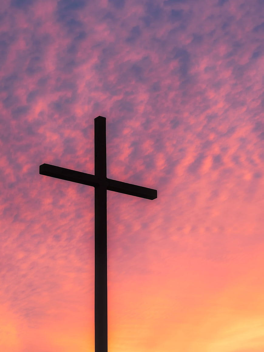 Silhouette of a Christian cross against a vibrant pink and orange sunset sky