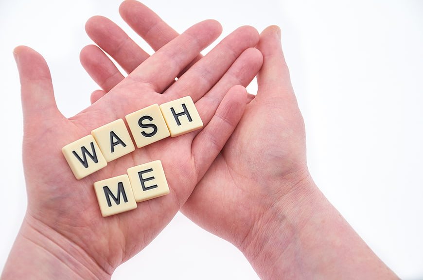 Hands holding Scrabble tiles spelling wash me on white background