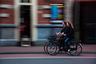 Two women riding bicycles in motion on city street
