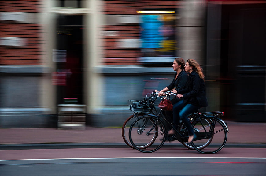 Two women riding bicycles in motion on city street