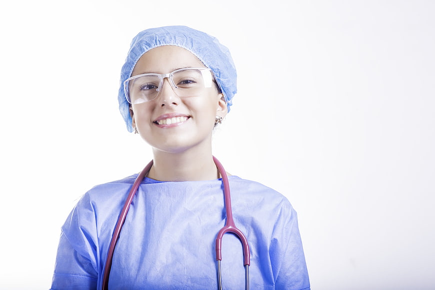 Smiling female surgeon in blue scrubs and safety glasses