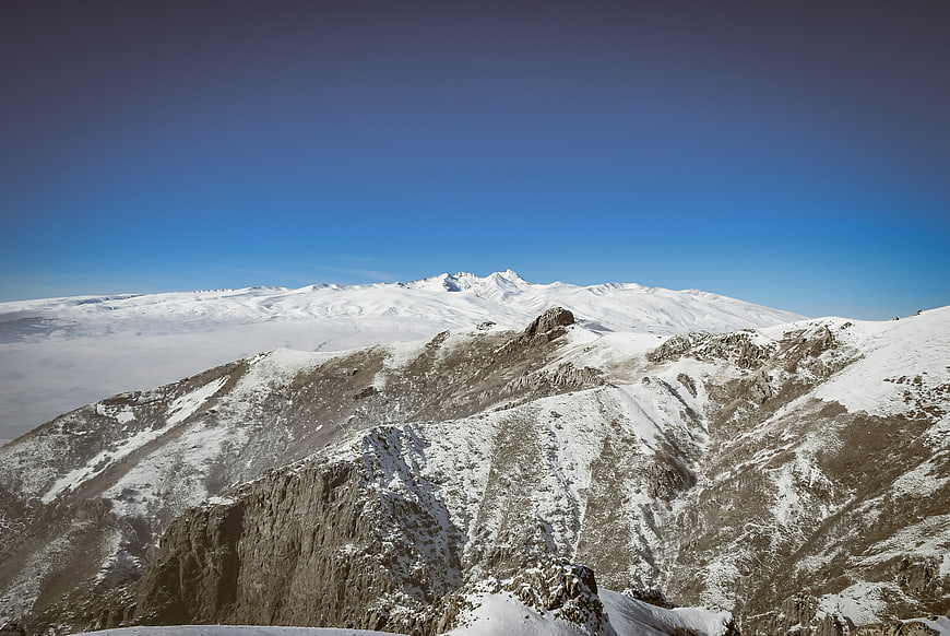 Snowy mountain peaks above clouds with blue sky