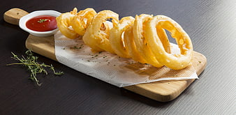 Golden fried onion rings with ketchup on a wooden serving board