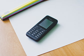 Black Nokia feature phone on white paper with colorful notebook