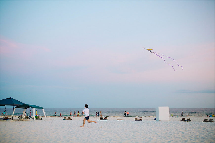 Man Running on Beach Flying Kite at Sunset