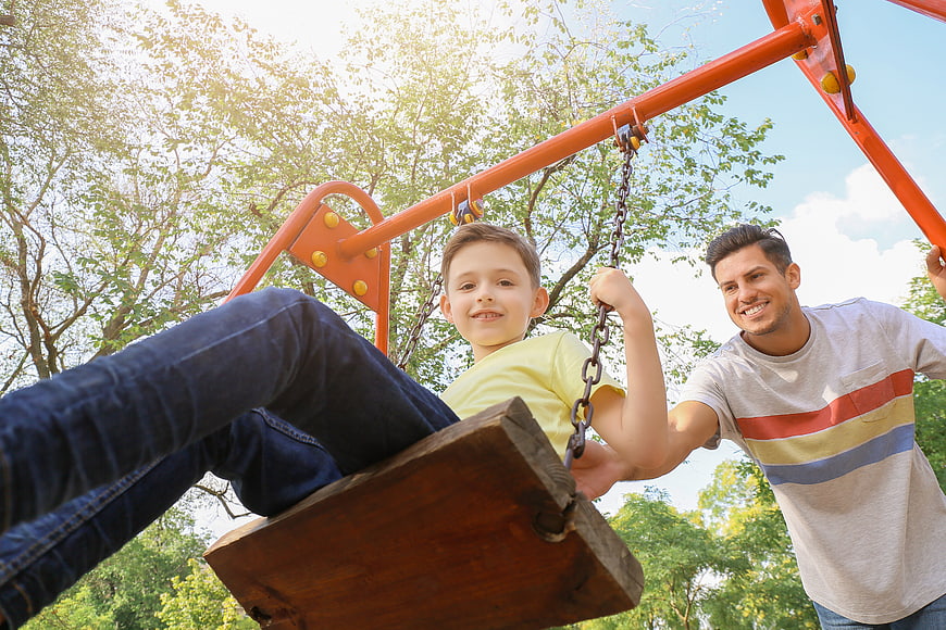 Father pushing smiling son on swing in sunny park