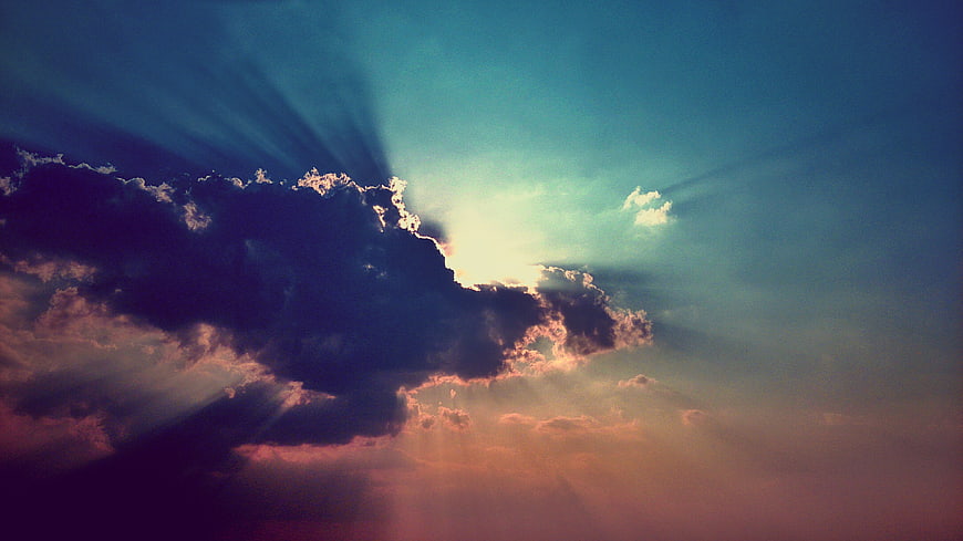 Dramatic sunset sky with sun rays breaking through dark clouds